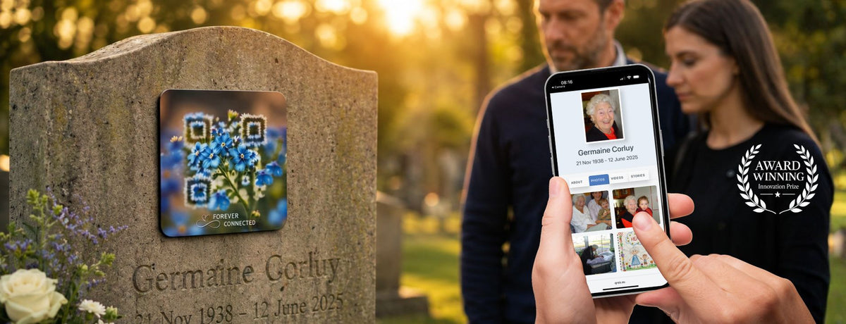 A square memorial plaque featuring a QR code artfully integrated into a blue forget-me-not floral design with the text "Forever Connected" at the bottom. The QR Plaque is attached to a stone headstone, with a hand in the foreground holding a smartphone displaying the deceased's digital profile page.