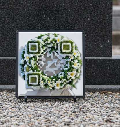 QR Memorial wreath with flowers and greenery on a pebbled surface.