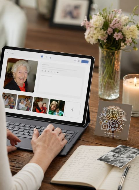 Person creating an online memorial page with photos and memories, next to a Forever Connected QR plaque and candle.