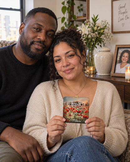 A man and a woman sitting together on a couch in a cozy living room setting. The woman holds up a square QR Plaque with a red poppies design