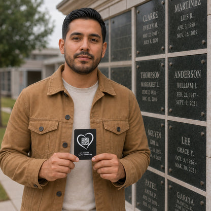 A man wearing a tan overshirt over a light gray t-shirt stands in front of a memorial wall, holding up a black square card with a white heart logo and QR code.